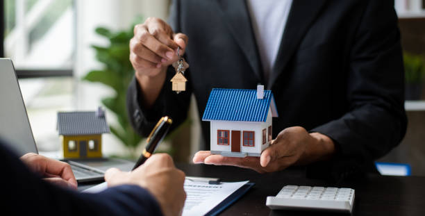 Hand presenting a house model with keys, for stated income loan approval